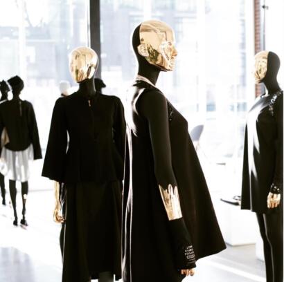 Display of mannequins in black outfits with metallic gold masks in a retail store window.