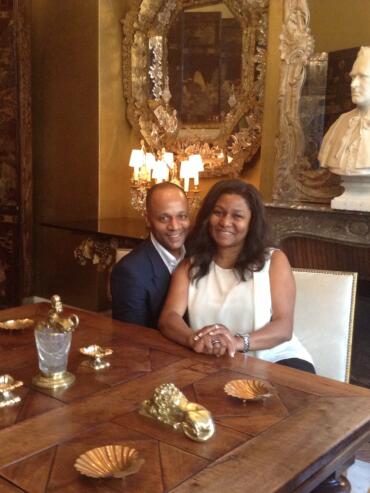 Elegant couple seated at a luxurious dining table in a richly decorated room with ornate mirrors and classical busts.
