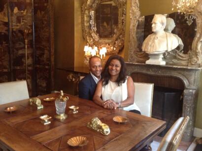 Elegant couple seated at a luxurious dining table in a richly decorated room with ornate mirrors and classical busts.