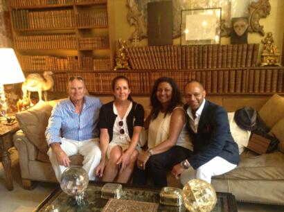Group of four people sitting on a sofa in an elegantly decorated library-style room, stylishly dressed.