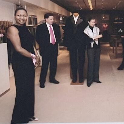 Group of people standing in a gallery or showroom, dressed in formal attire.