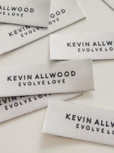 Clothing labels reading "Kevin Allwood Evolve Love" scattered on a white surface.
