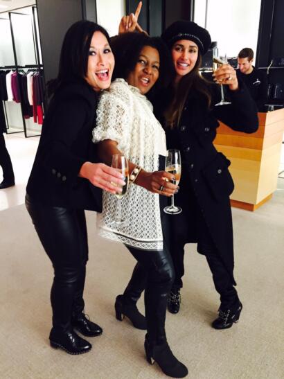 Three women celebrating and holding champagne glasses, dressed stylishly for an event.
