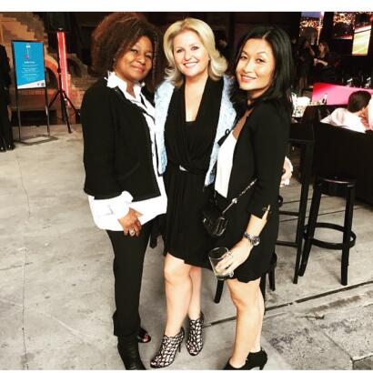 Three women dressed in stylish black and white outfits, posing at a social event.