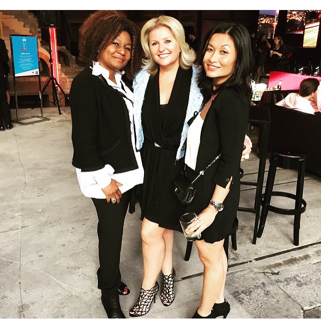 Three women dressed in stylish black and white outfits, posing at a social event.