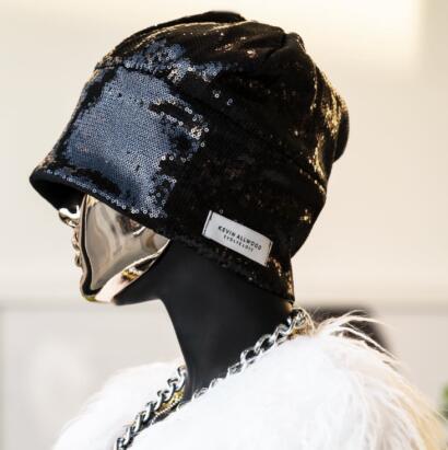 Black sequined beanie with "Kevin Allwood" label, styled with a chunky chain necklace.
