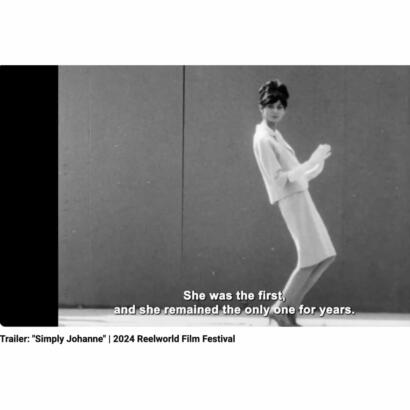 Black-and-white still of a woman in 1960s fashion, standing against a plain background.