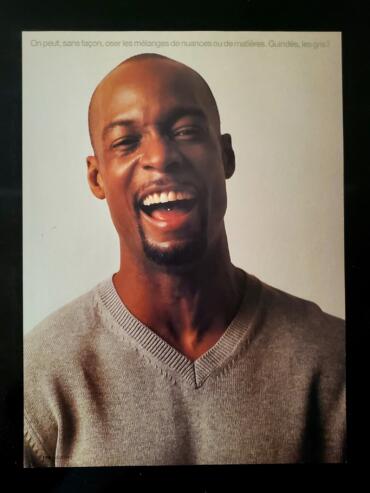 Close-up of a smiling man with a shaved head and goatee, wearing a grey V-neck sweater.