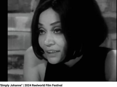 Black-and-white image of a woman with a voluminous bob hairstyle, wearing a sleeveless top, captured in a cinematic style.