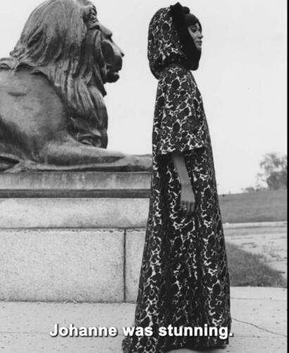 A woman in a patterned outfit standing beside a stone lion sculpture in a black and white photo.