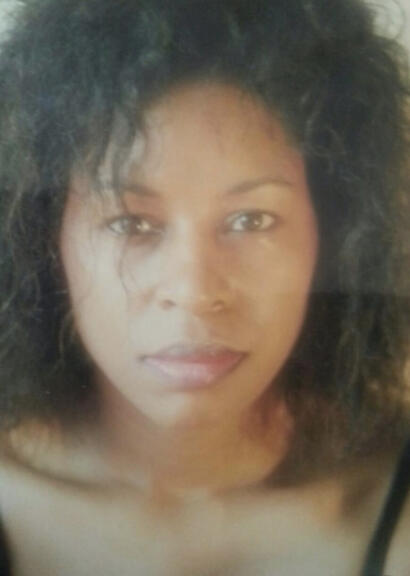 A close-up portrait of a woman with curly black hair, glowing skin, and subtle makeup.