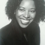 Black-and-white portrait of a woman with curly hair, smiling and wearing a dark top.