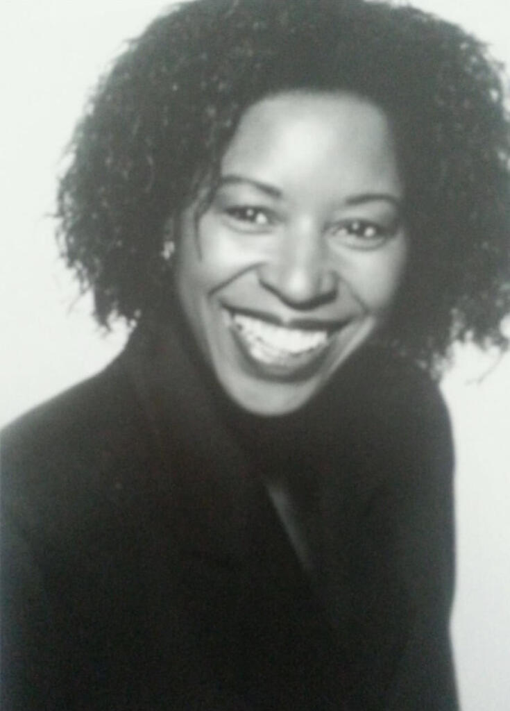 Black-and-white portrait of a woman with curly hair, smiling and wearing a dark top.