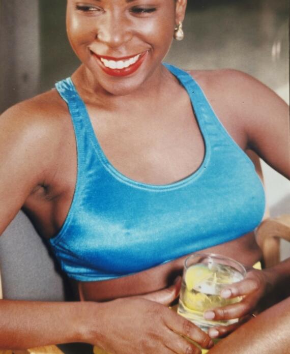 Woman smiling, wearing a blue crop top and holding a glass of lemon-infused water.