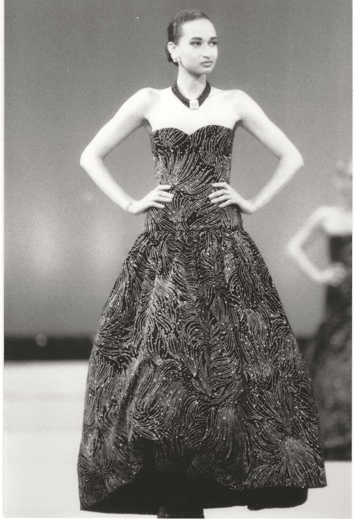 Elegant black evening gown with intricate feather-like patterns, accessorized with a statement necklace.