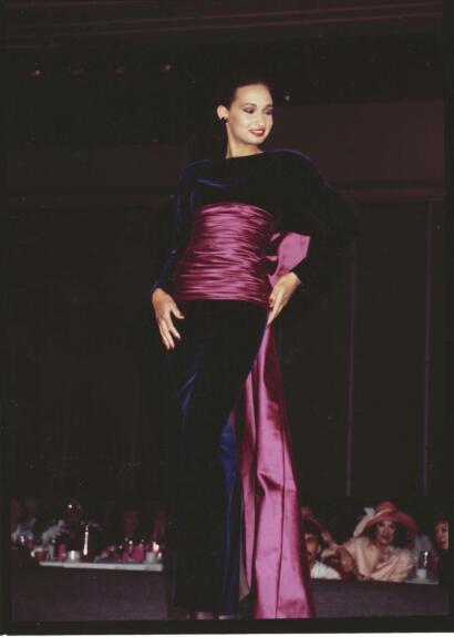 Model walking the runway in a velvet gown with satin accents, showcasing elegant evening wear.