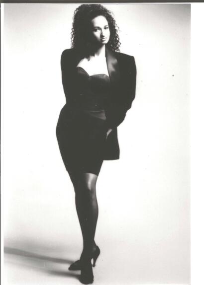 Black-and-white image of a woman in an elegant outfit, standing confidently.