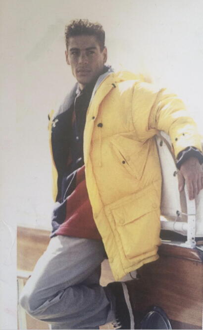 Young man in a yellow jacket and layered clothing, posing casually indoors.