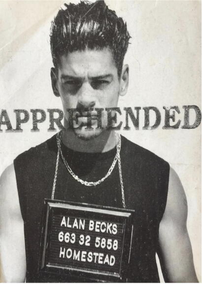 Black and white photo of a young man with styled hair, wearing layered necklaces and a sleeveless top, with "APPREHENDED" stamped across his face and a sign with contact details and location.