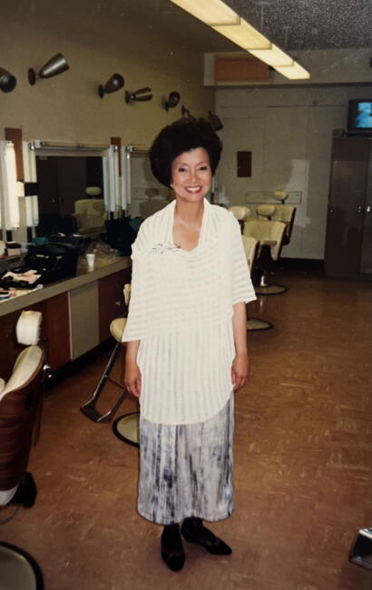 Woman with a voluminous black hairstyle, wearing a white striped top and a patterned skirt, standing in a vintage dressing room.