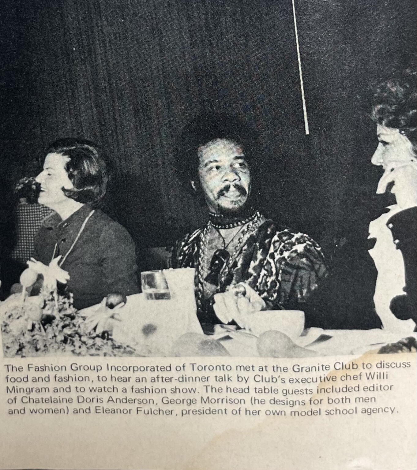Black-and-white photo of three people at a table during a fashion event in Toronto.