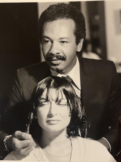 Black-and-white photo of a man in a suit and a woman with wet hair, with the man smiling and the woman closing her eyes.