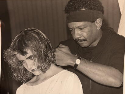 A hairstylist styles a woman's curly haircut in a classic black-and-white photograph.