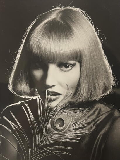 Black and white portrait of a woman with a bob haircut holding a peacock feather.