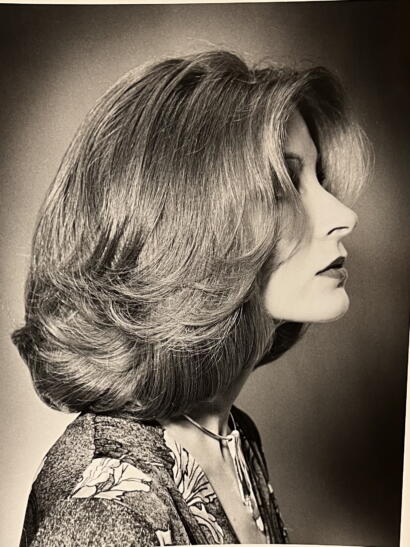 Elegant black-and-white portrait of a woman with voluminous, layered hairstyle and vintage-inspired attire.