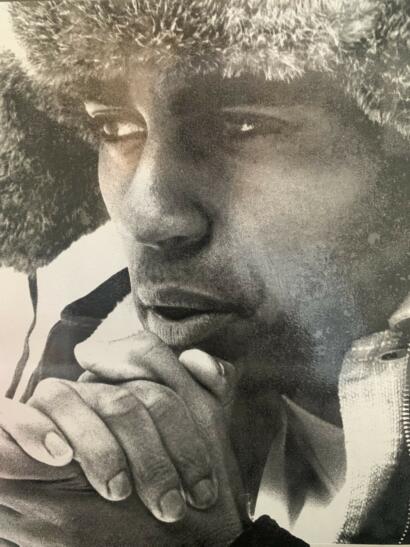 Close-up portrait of a person with textured hair, resting their chin on intertwined hands.