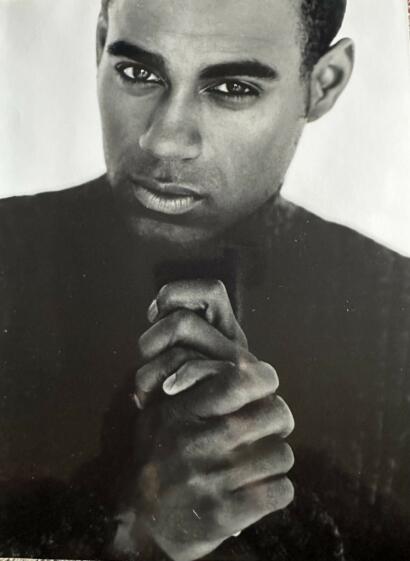 Close-up black and white portrait of a man with intense expression, clasped hands, and short hair.
