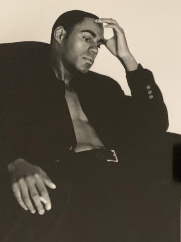 Black and white portrait of a young man with short hair, wearing a partially open jacket, sitting thoughtfully.