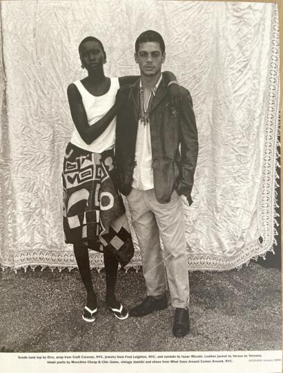 A stylish duo posed against a textured backdrop, showcasing 1998 fashion with jewelry, leather, and bold patterns.