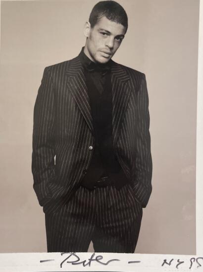 Black and white portrait of a young man in a pinstripe suit with hands in pockets, exuding confidence.