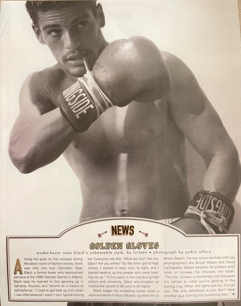Black-and-white photo of a shirtless male boxer, wearing gloves, with one fist extended.