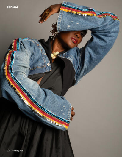 Model wearing a denim jacket with colorful embellishments and a black dress, striking a pose.