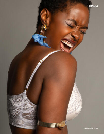 Close-up of a joyful woman with short hair, wearing a lace top, colorful earrings, and a gold arm cuff.