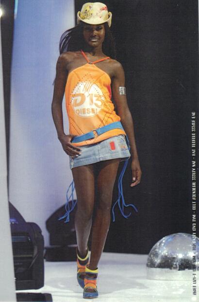 Model walking runway in colorful, sporty fashion with hat and trendy accessories.