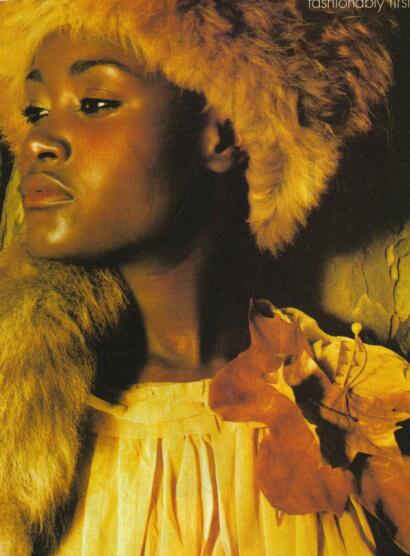 Close-up of a woman with a fur hood, amber-toned makeup, and a yellow dress.