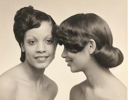 Black and white portrait of two women with vintage hairstyles, one smiling at the camera, the other showing a side profile.