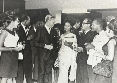 Elegant guests mingle at a formal event, dressed in vintage black-tie attire.