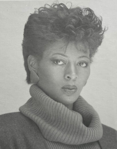 Black and white portrait of a woman with short, curly hair, wearing a turtleneck sweater.
