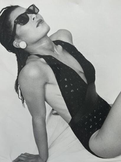 Black and white image of a woman in sunglasses, wearing a lace top and large earrings, posing confidently.
