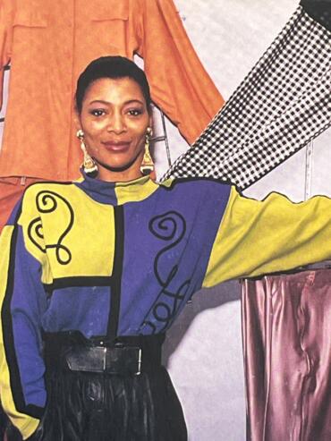Elegant woman in a colorful abstract-patterned top, accessorized with earrings, standing indoors.