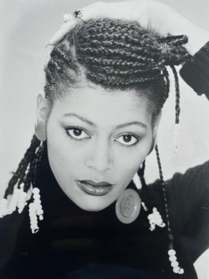 Black and white portrait of a woman with styled dreadlocks, wearing earrings and a buttoned-neck top.