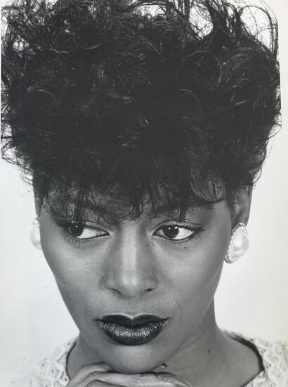 Black and white portrait of a woman with short, curly hair, bold makeup, and pearl earrings.