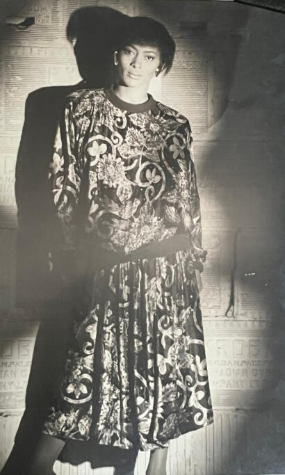 A woman in a patterned dress posing against a vintage, textured wall.