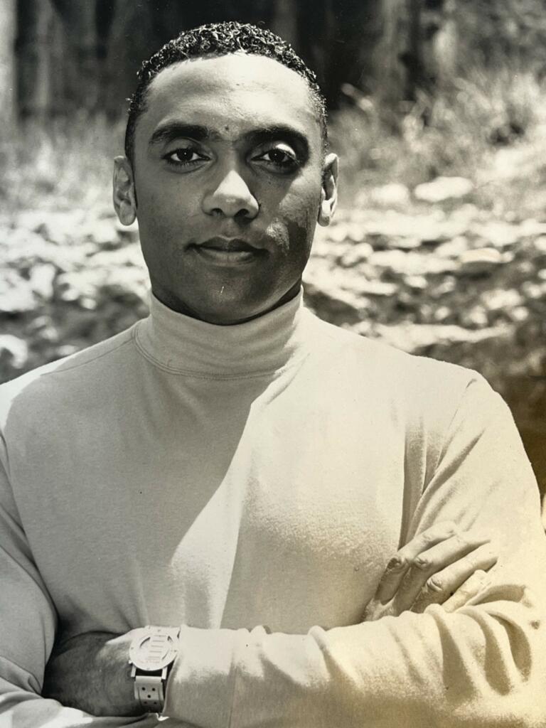 Male model in a turtleneck, with crossed arms, outdoors in black and white.