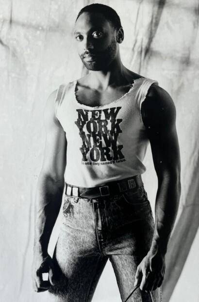 Black-and-white street style portrait of a person in a torn "New York" tank top and high-waisted jeans.
