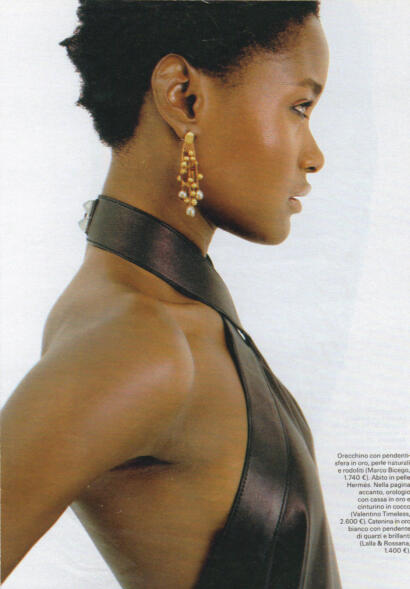Elegant side profile of a woman wearing pearl and gold drop earrings, dark leather outfit, and gold jewelry.